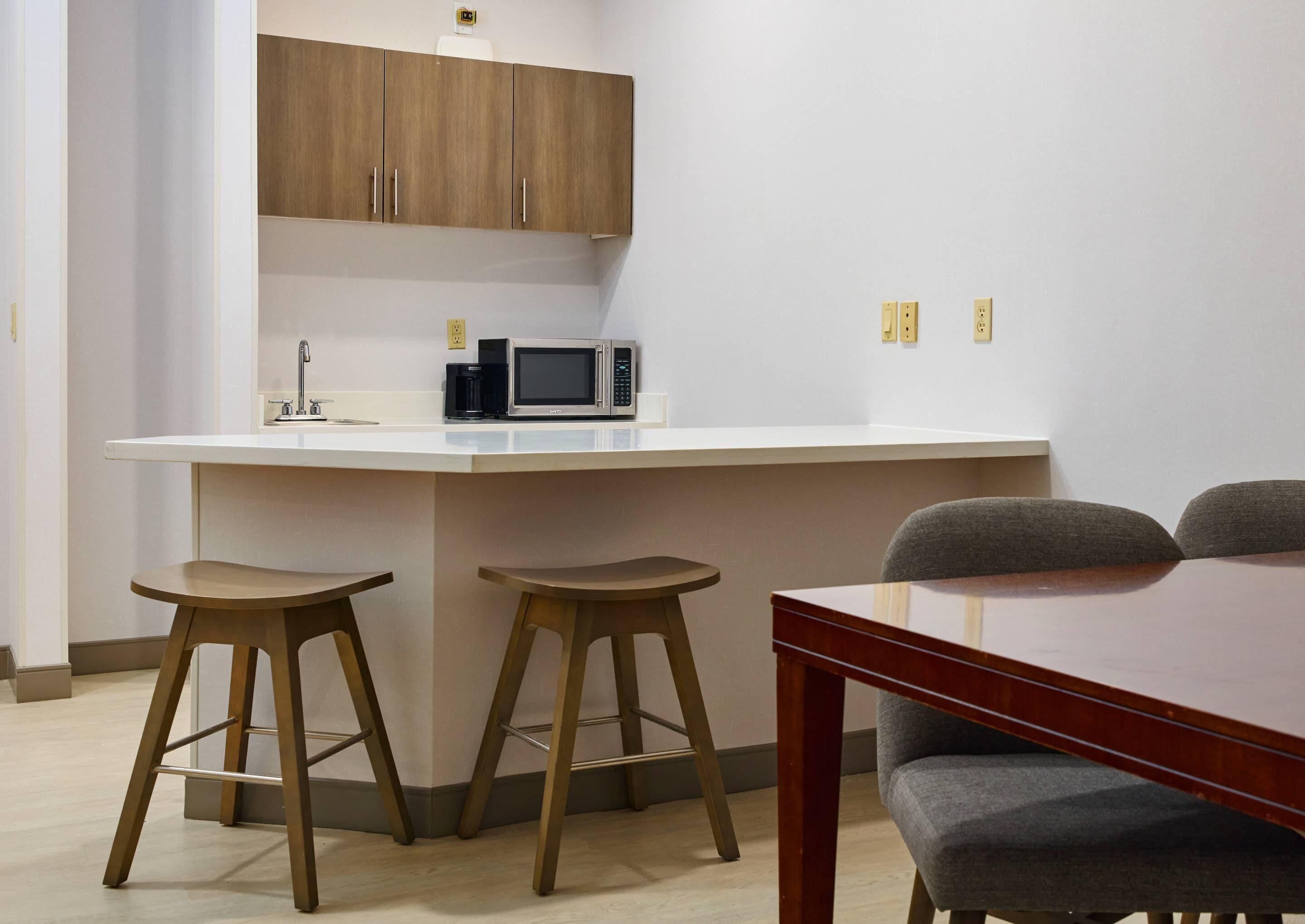A compact kitchen with a microwave, two stools, and a wooden table.