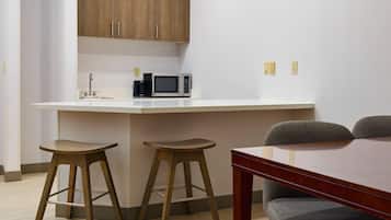 A compact kitchen with a microwave, two stools, and a wooden table.