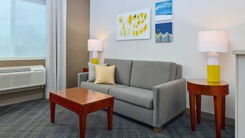 A hotel room with a grey sofa, a wooden coffee table, two bedside lamps, and artwork on the wall.