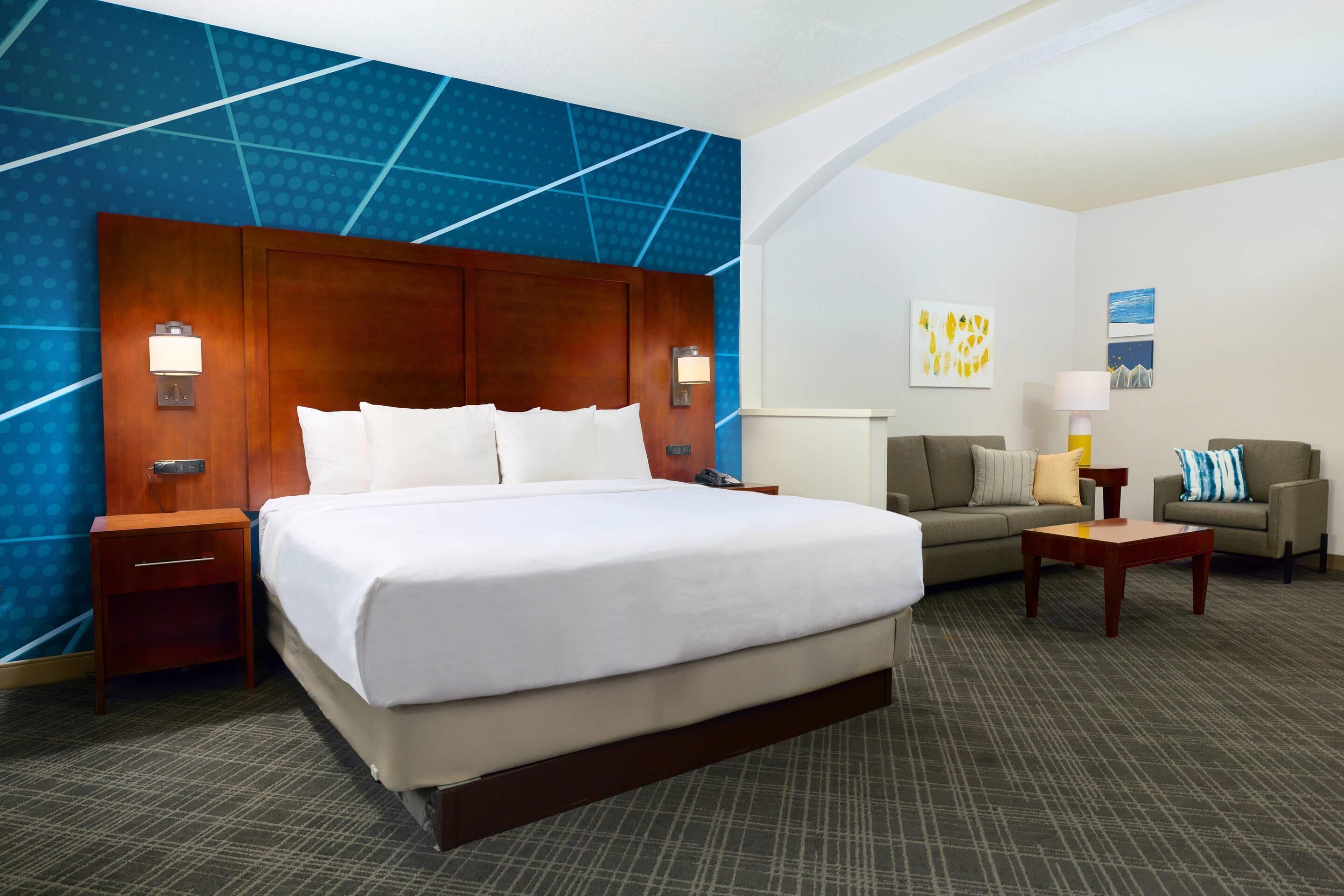 A hotel room with a large bed, a sofa, a small table, and a nightstand.