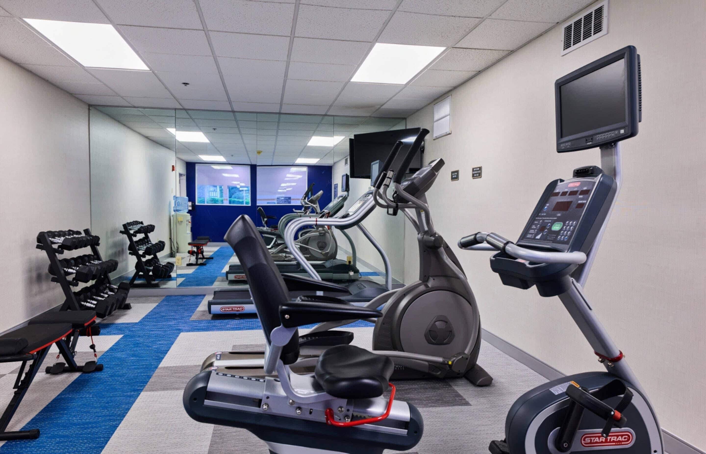 Un gimnasio con cintas de correr, elípticas y bancos de pesas.