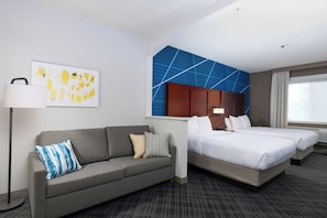 A hotel room with a grey sofa, two beds, a blue accent wall, and artwork on the wall. - Comfort Suites Springfield-Eugene (Springfield)