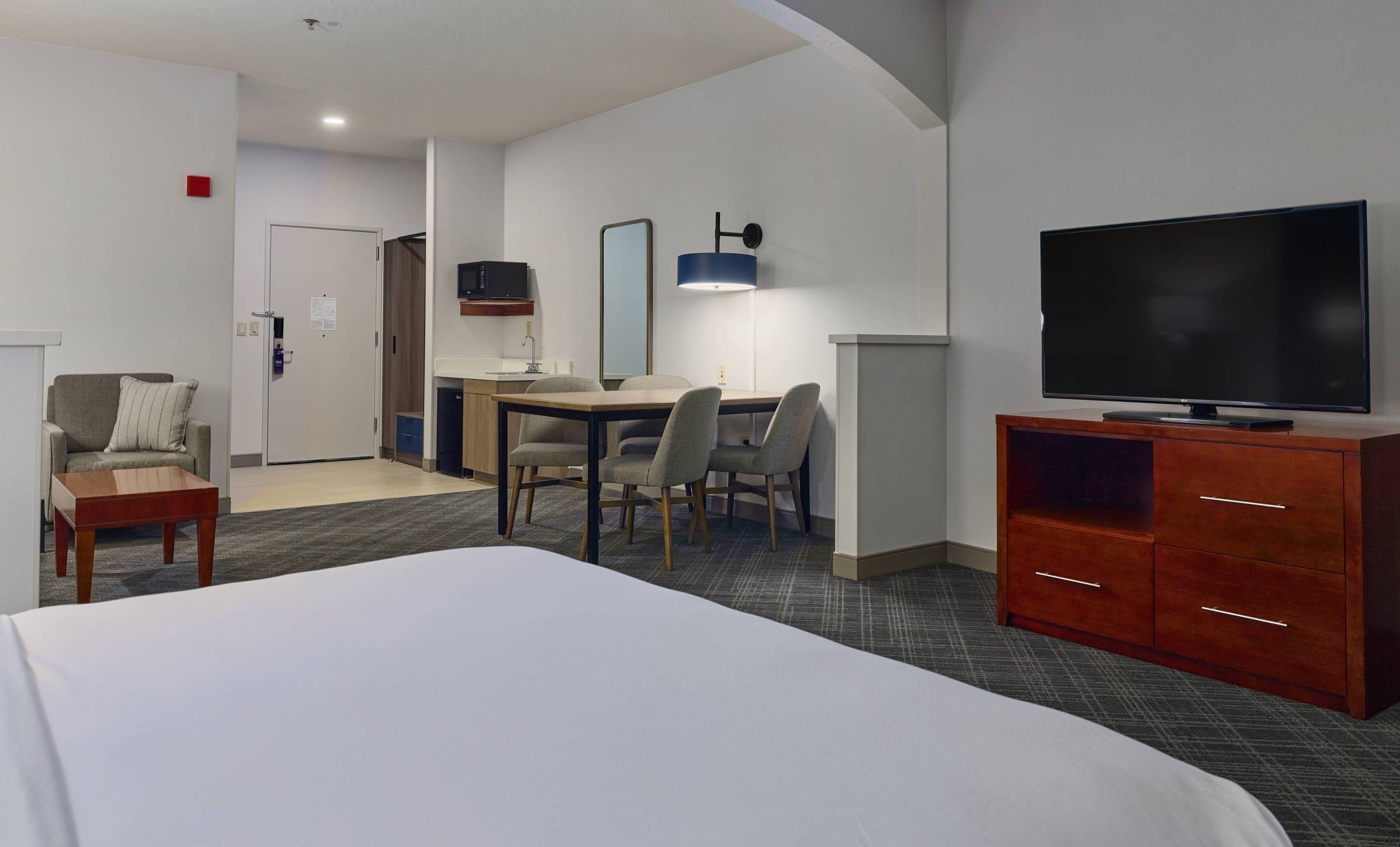 A hotel room with a bed, a desk with a chair, a television, and a wardrobe.