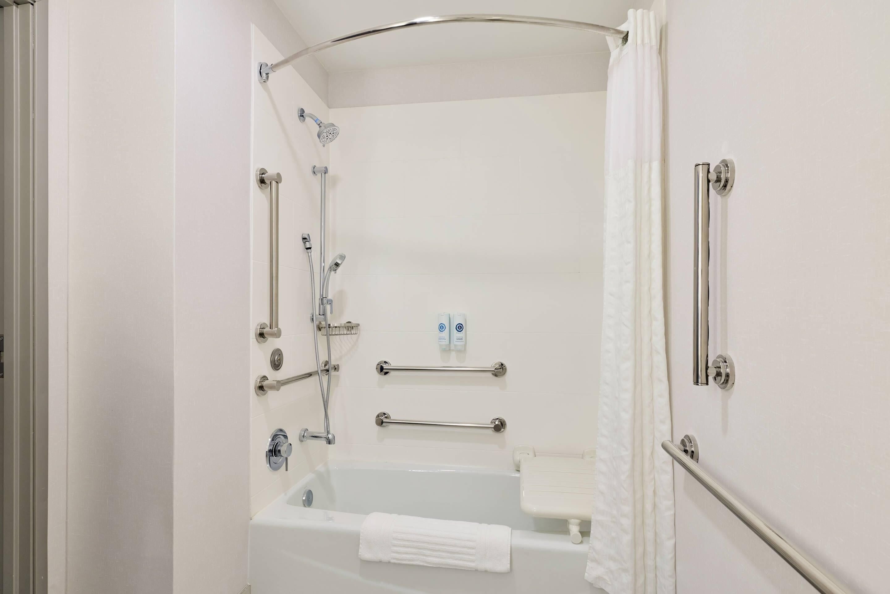 A bathroom with a bathtub, a shower, and grab bars.