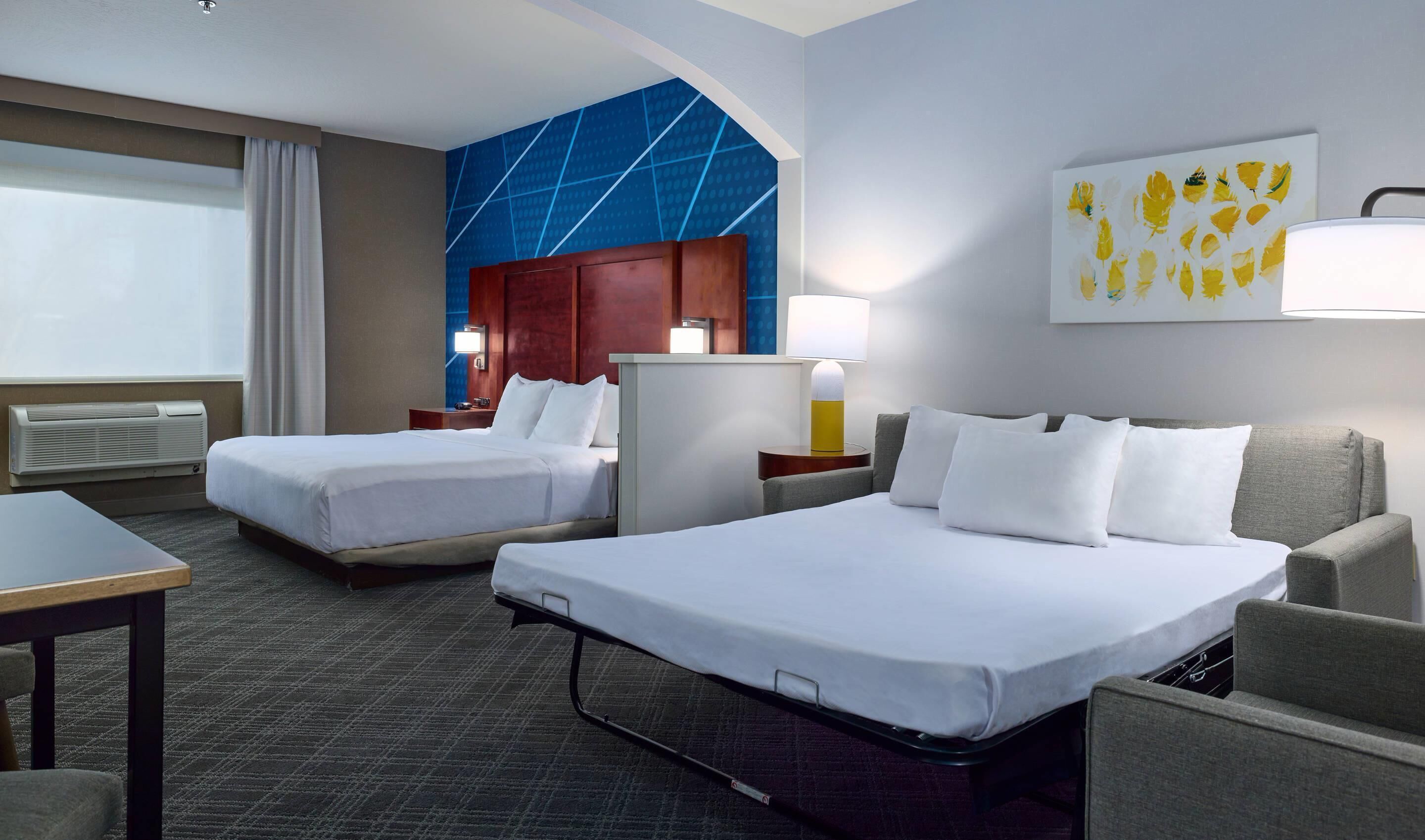 Habitación de hotel con dos camas, un escritorio, una silla, una lámpara y una pared con diseño geométrico.