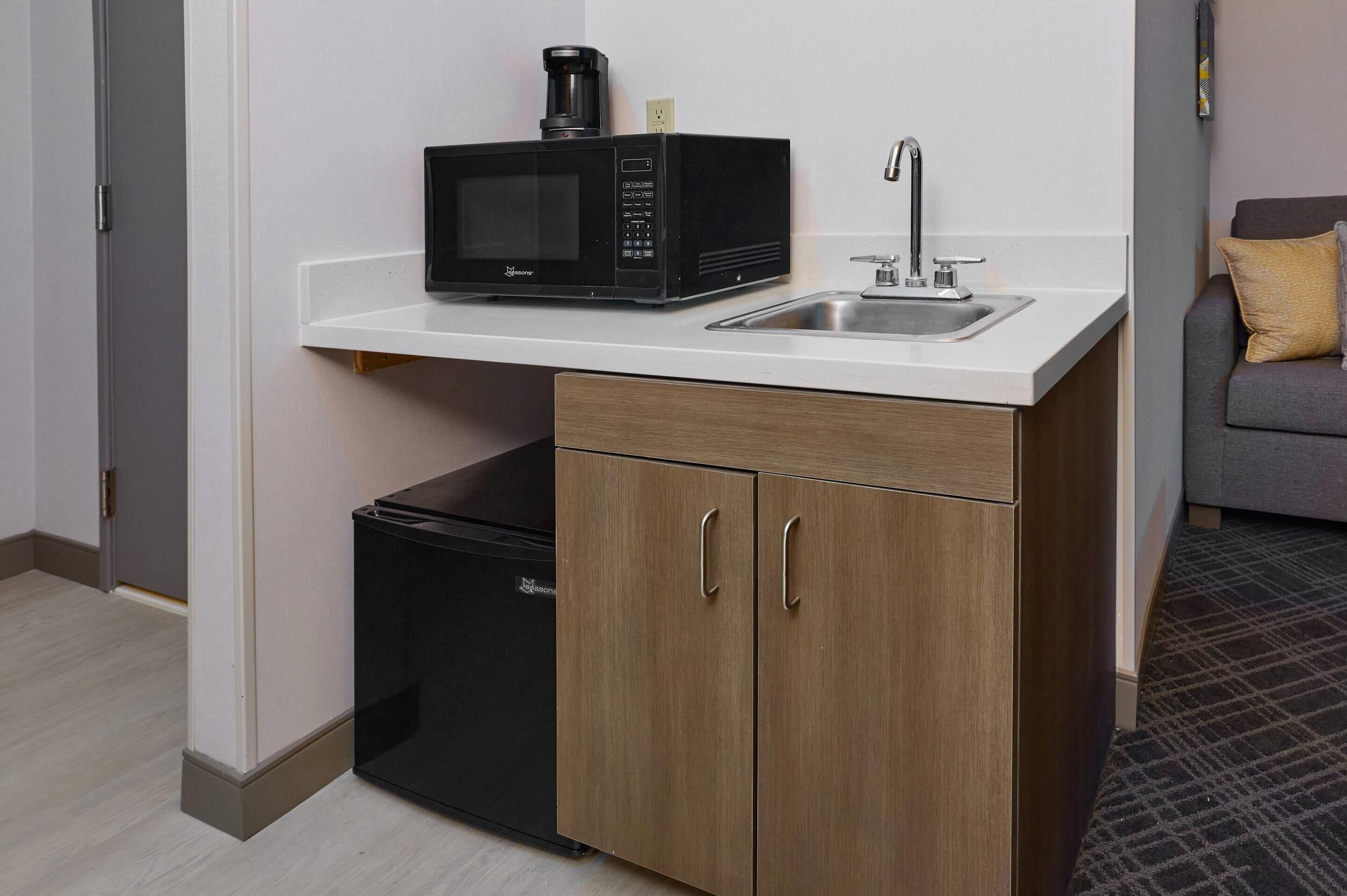 Una kitchenette compacta con microondas, pileta y un pequeño refrigerador.