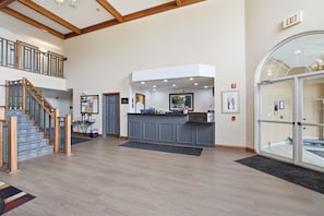 A hotel lobby with a reception desk, a staircase, and a glass door entrance. - The Commerce, Trademark Collection by Wyndham (River Falls)