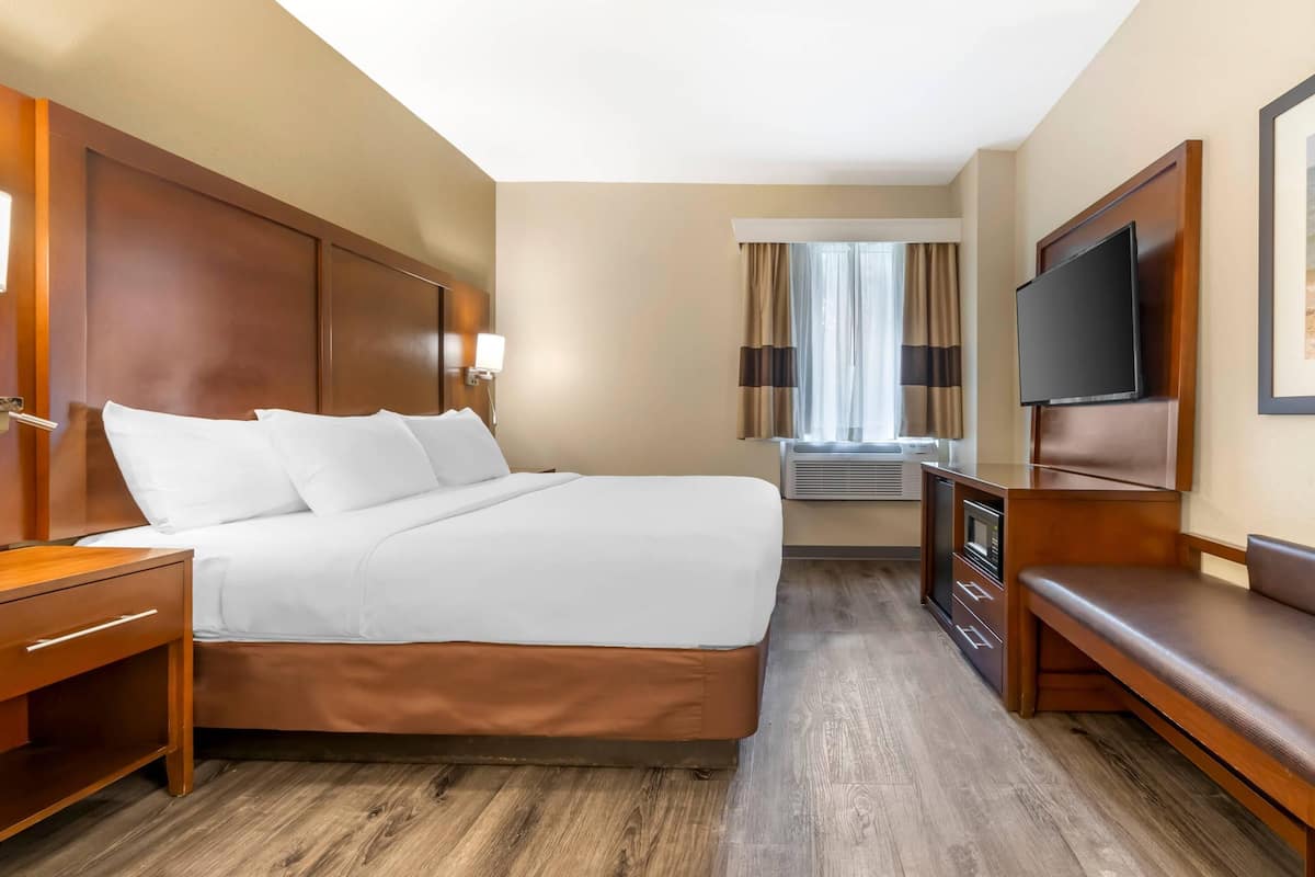A hotel room with a bed, a TV, a desk, and a window with curtains.
