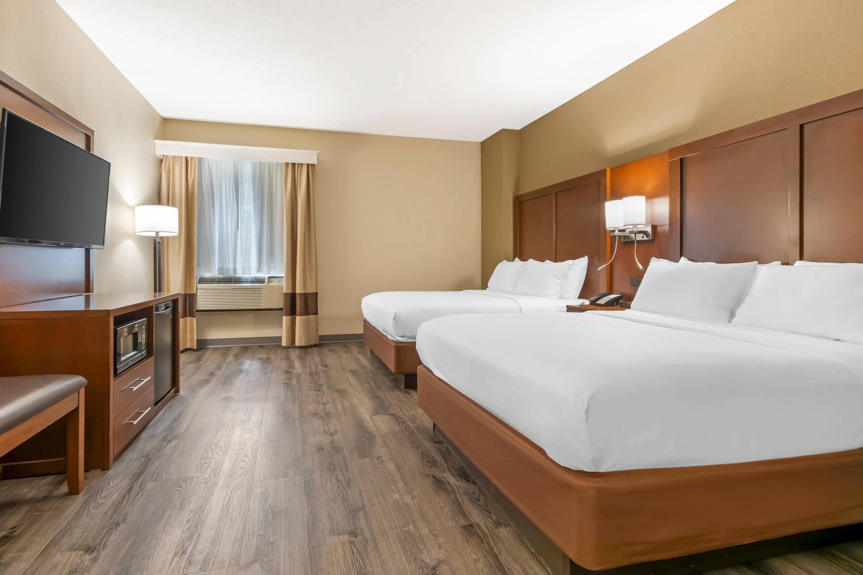 Habitación de hotel con televisión, dos camas, escritorio y lámpara.