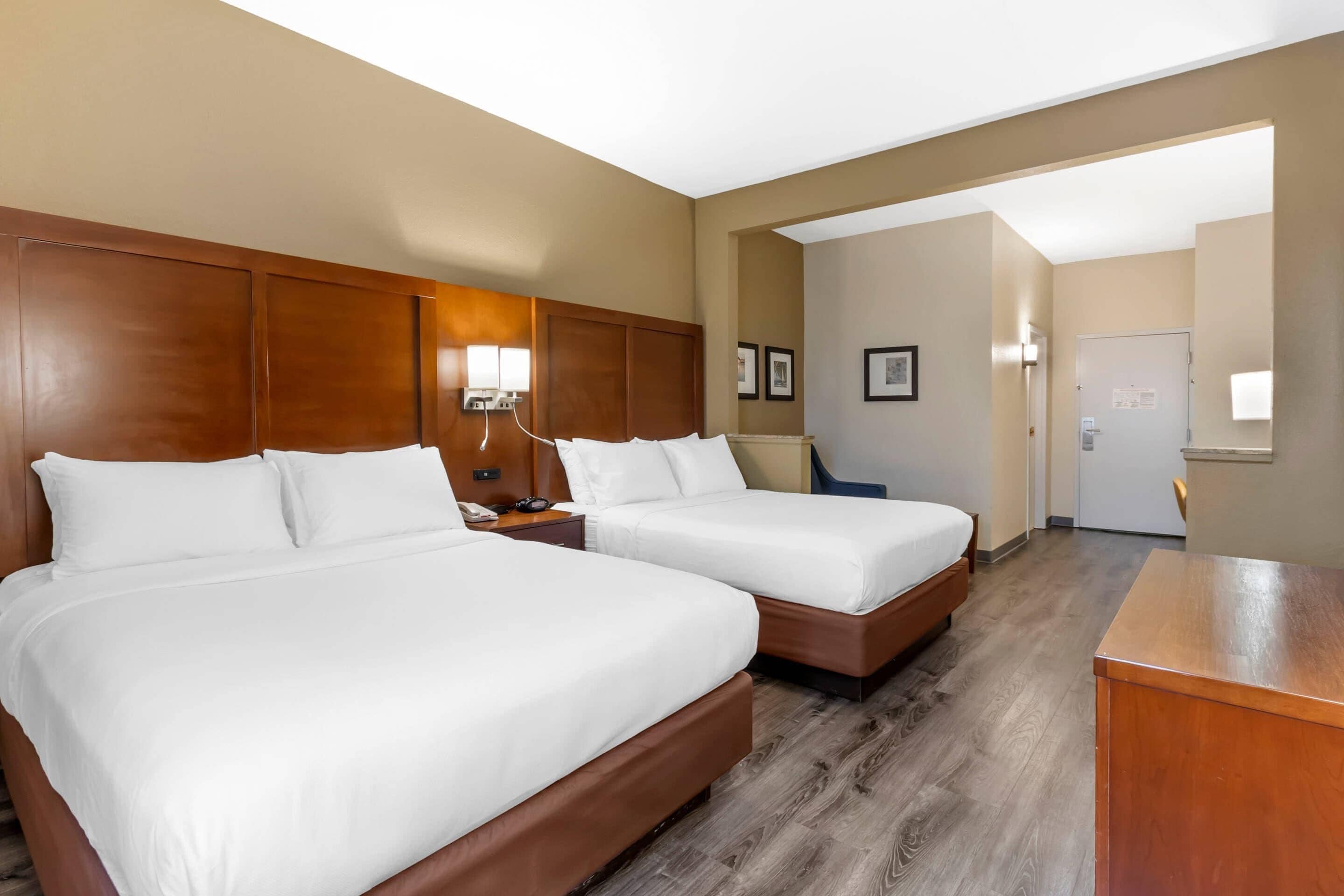 Habitación de hotel con dos camas, cabecero de madera, escritorio, una silla y una puerta.