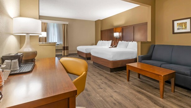 A hotel room with a wooden desk, two single beds, a sofa, and a large window. - Comfort Suites At The University - Conway (Conway)