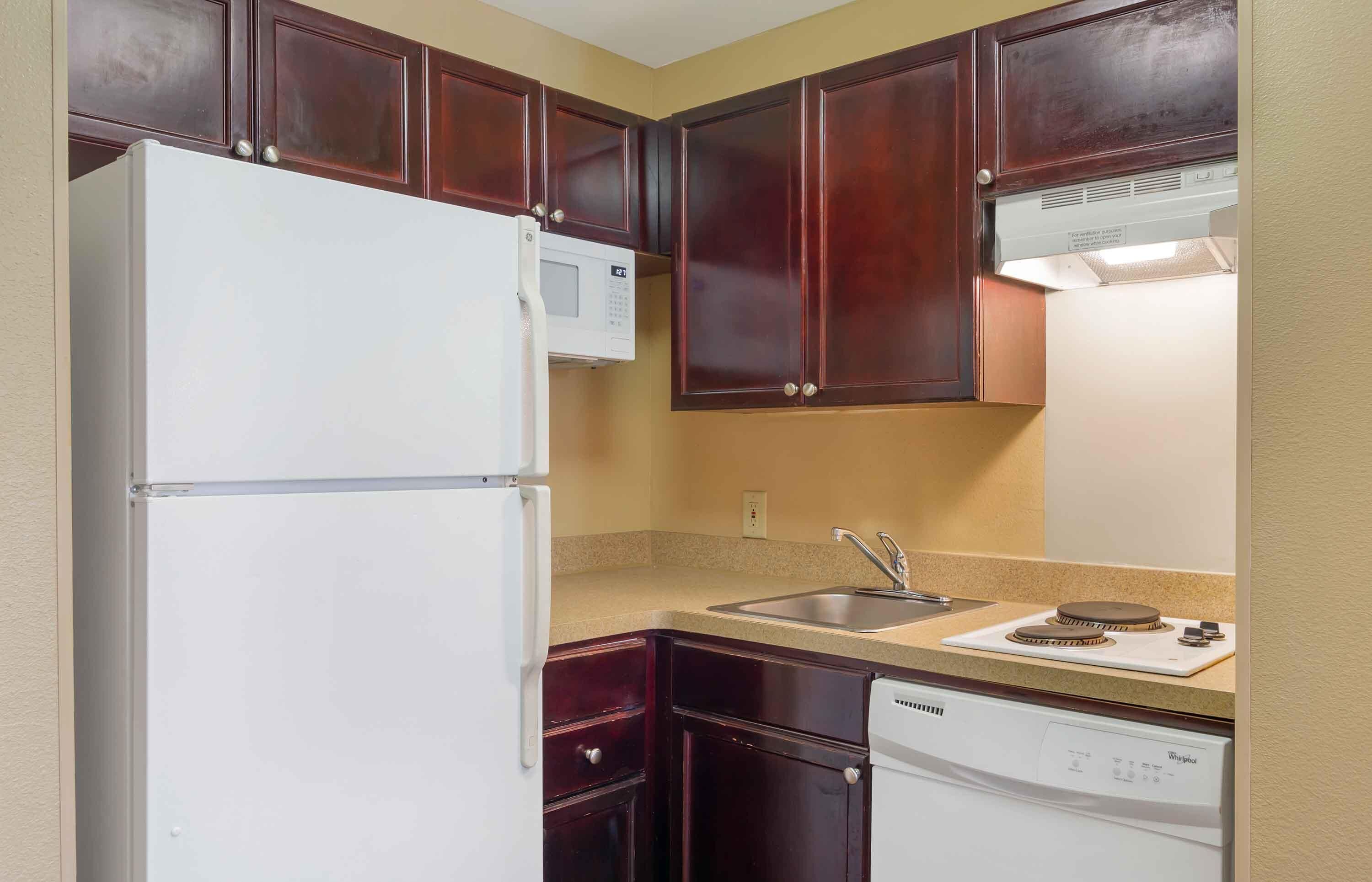 A compact kitchen with dark wooden cabinets, a white refrigerator, a microwave, a sink, and a dishwasher.