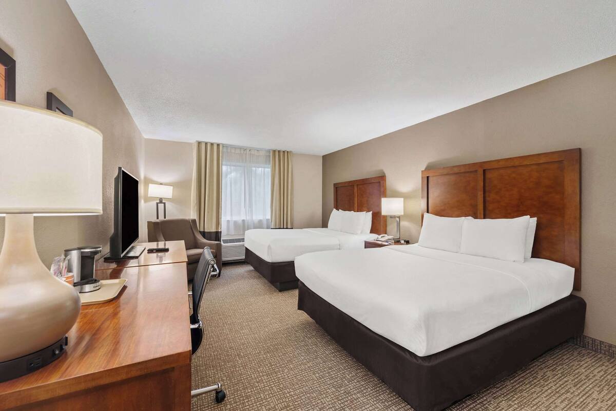A hotel room with two beds, a desk with a lamp, a TV, and a window with curtains.