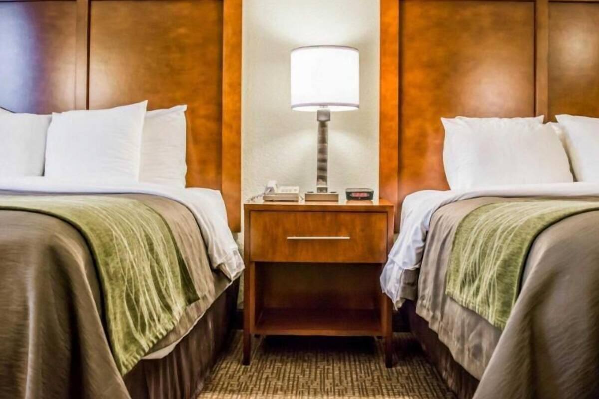 A hotel room with two beds, a nightstand with a lamp, and a telephone.