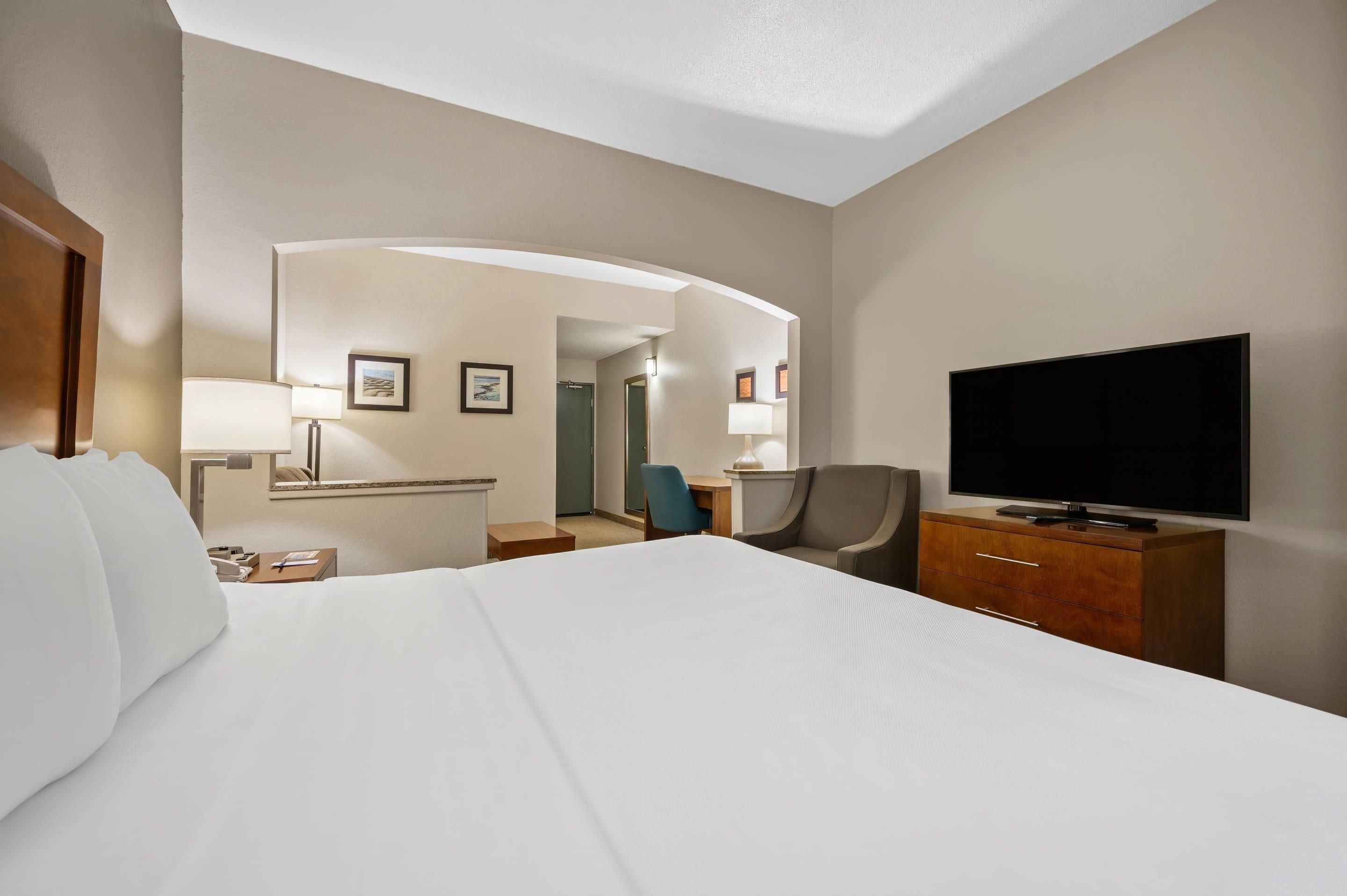 A hotel room with a bed, a television, a desk with a lamp, a chair, and a mirror.