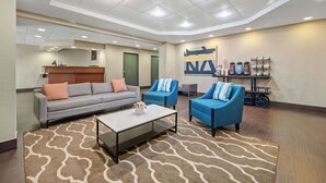 A modern lobby with a grey sofa, two blue armchairs, a coffee table, and a wall-mounted shelf with various items. - Comfort Inn Fort Myers Northeast (Fort Myers)