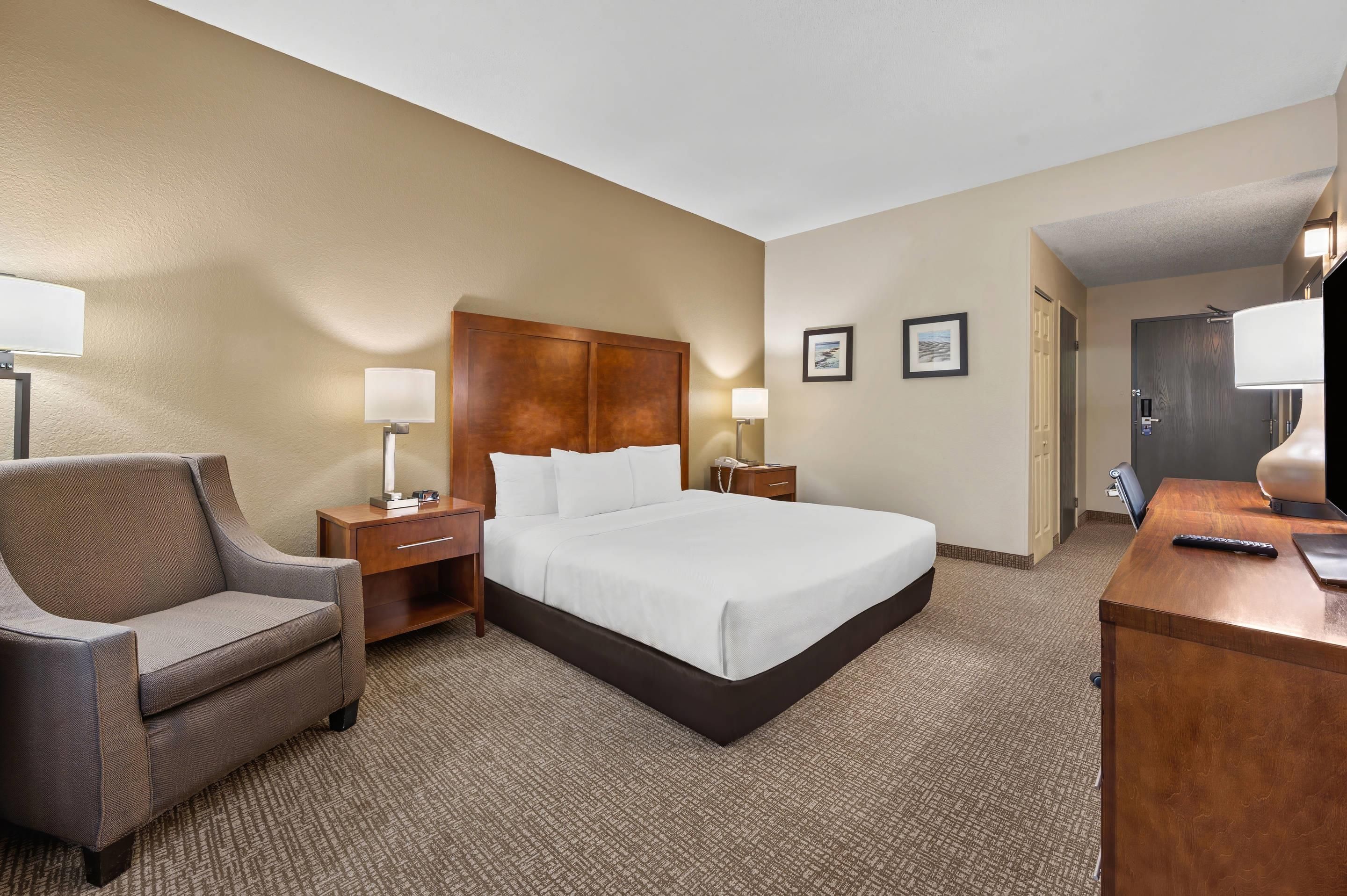A hotel room with a bed, a chair, a desk, and two bedside lamps.