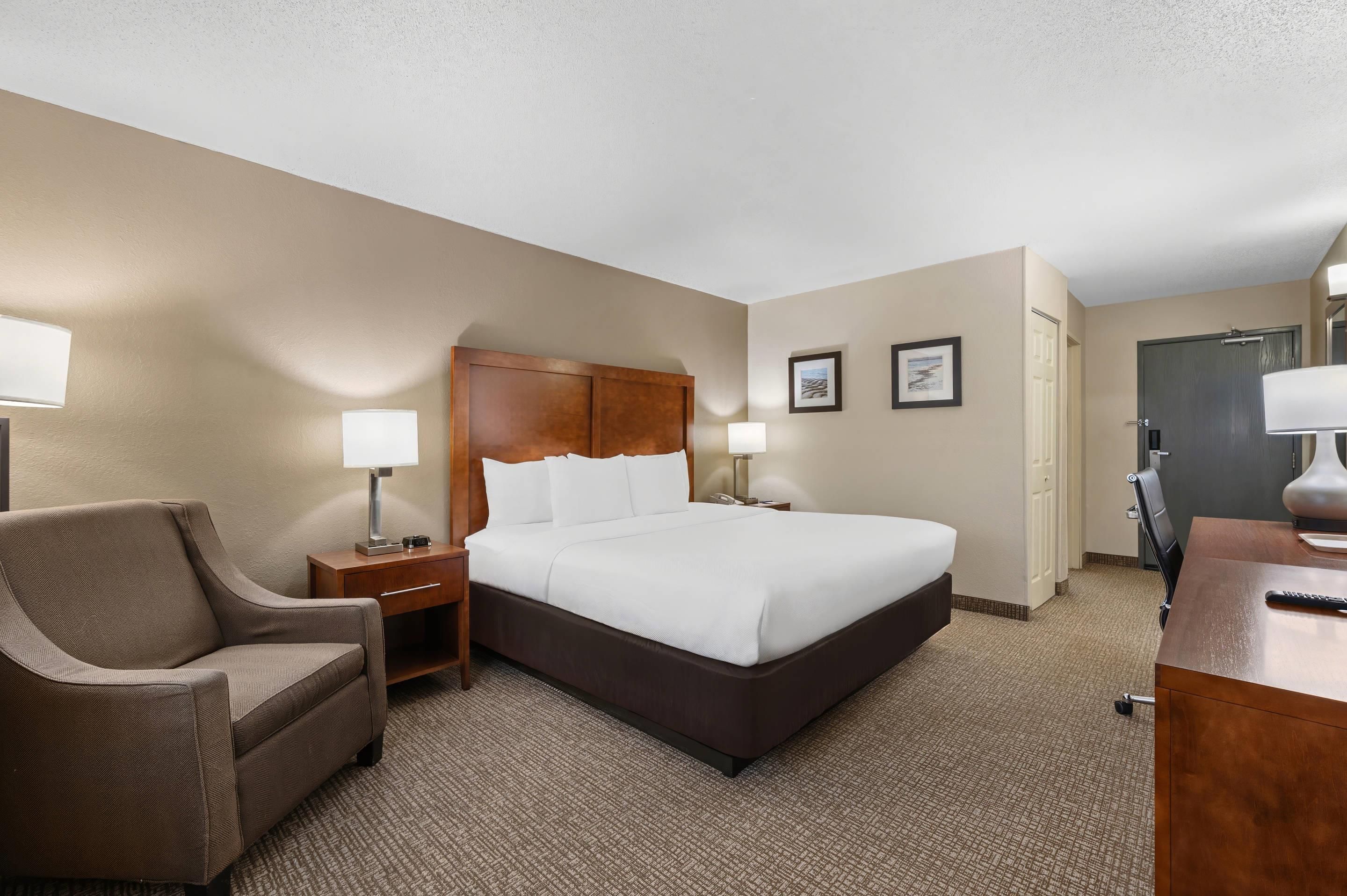 Ein Hotelzimmer mit einem Bett, einem Sessel, einem Schreibtisch und einer Tür.