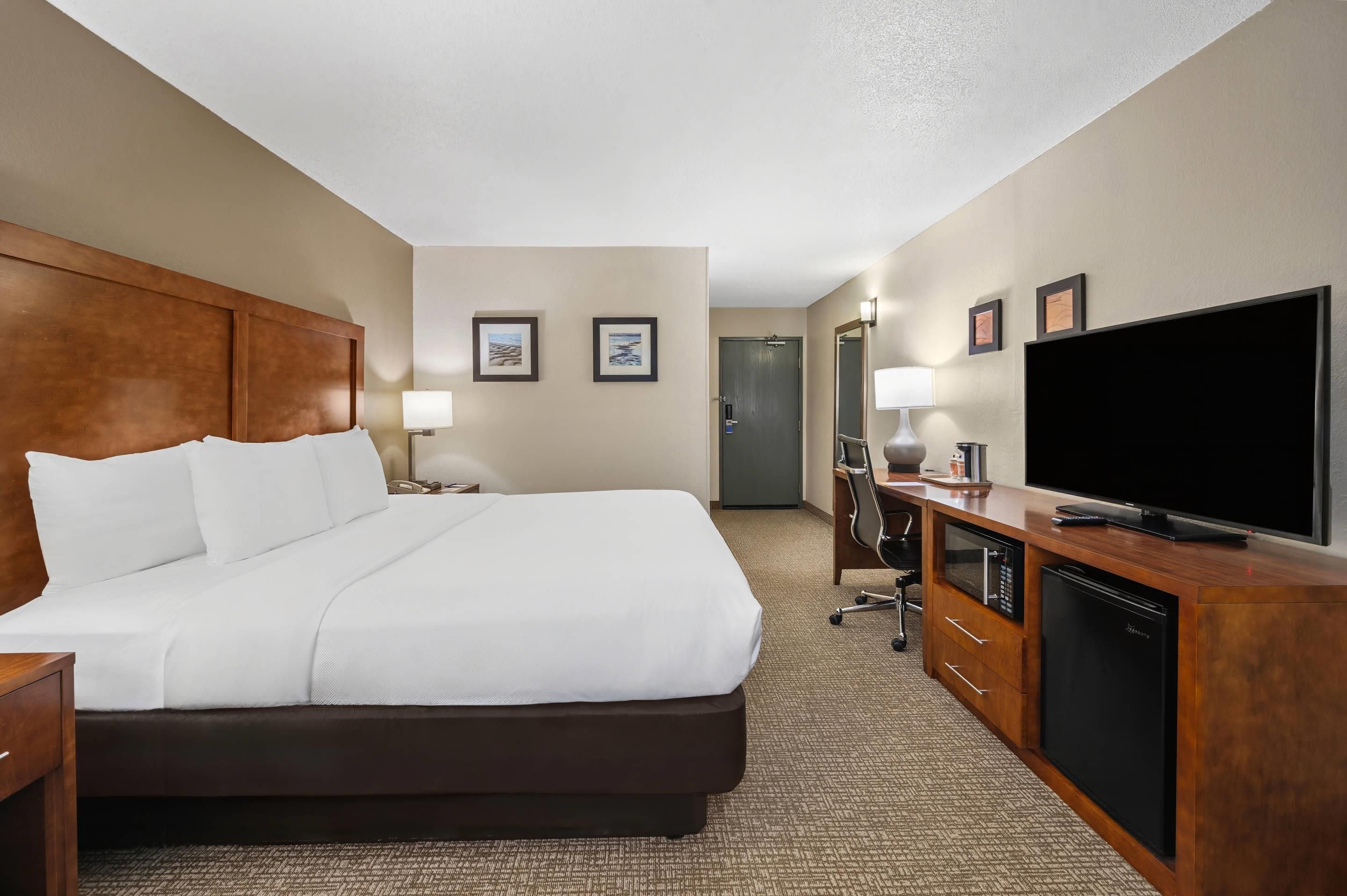 A hotel room with a large bed, a flat-screen TV, a desk with a computer, and a microwave.