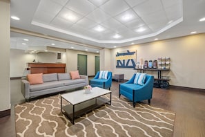 A modern lounge area with a sofa, two armchairs, a coffee table, and a wall-mounted coffee station. - Comfort Inn Fort Myers Northeast (Fort Myers)