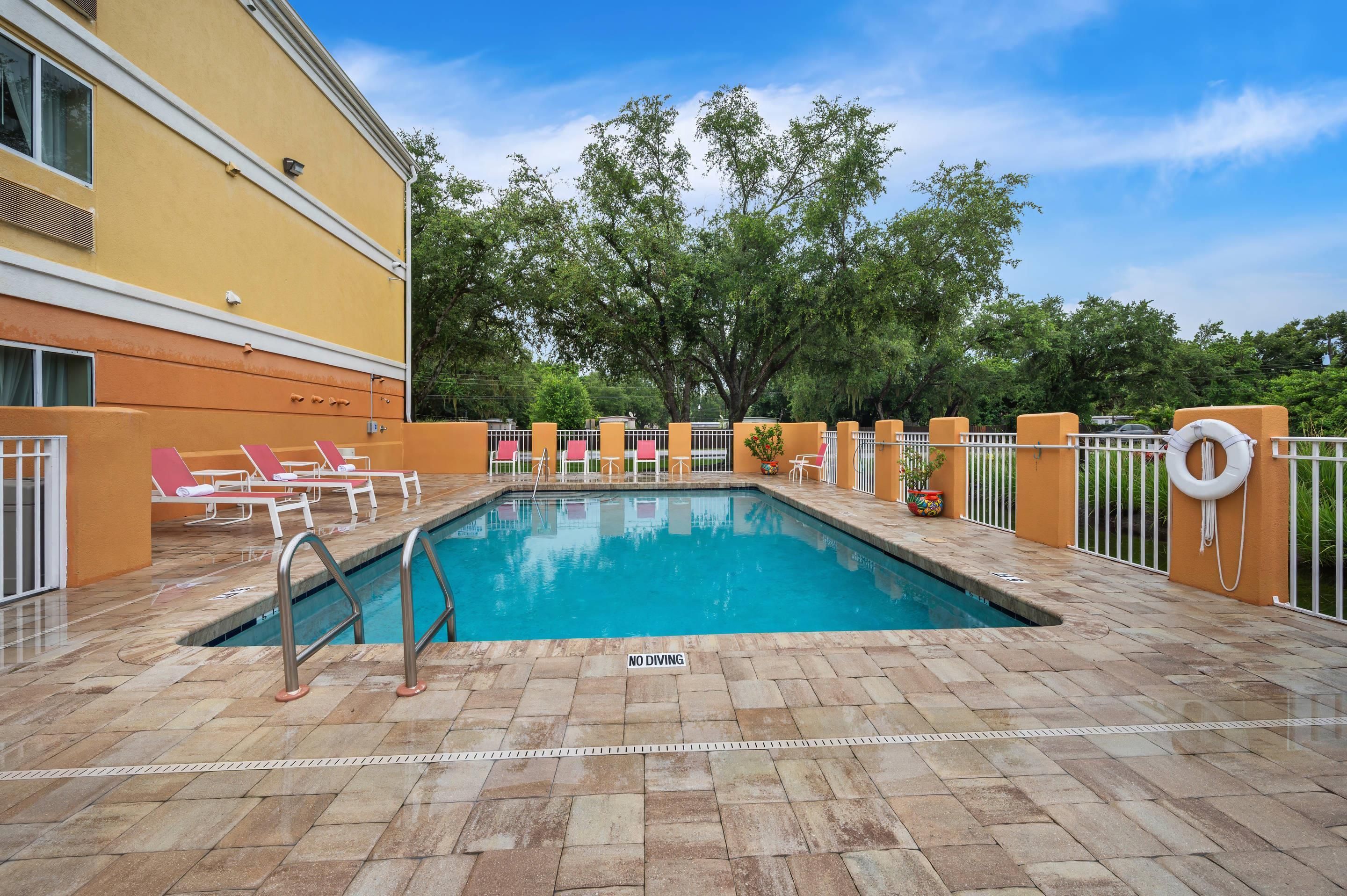 A rectangular pool with a no diving sign, surrounded by lounge chairs and potted plants.