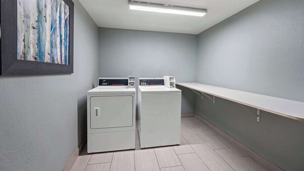A laundry room with two front-loading washers and dryers, a long counter, and a framed abstract painting on the wall. - Comfort Inn Fort Myers Northeast (Fort Myers)