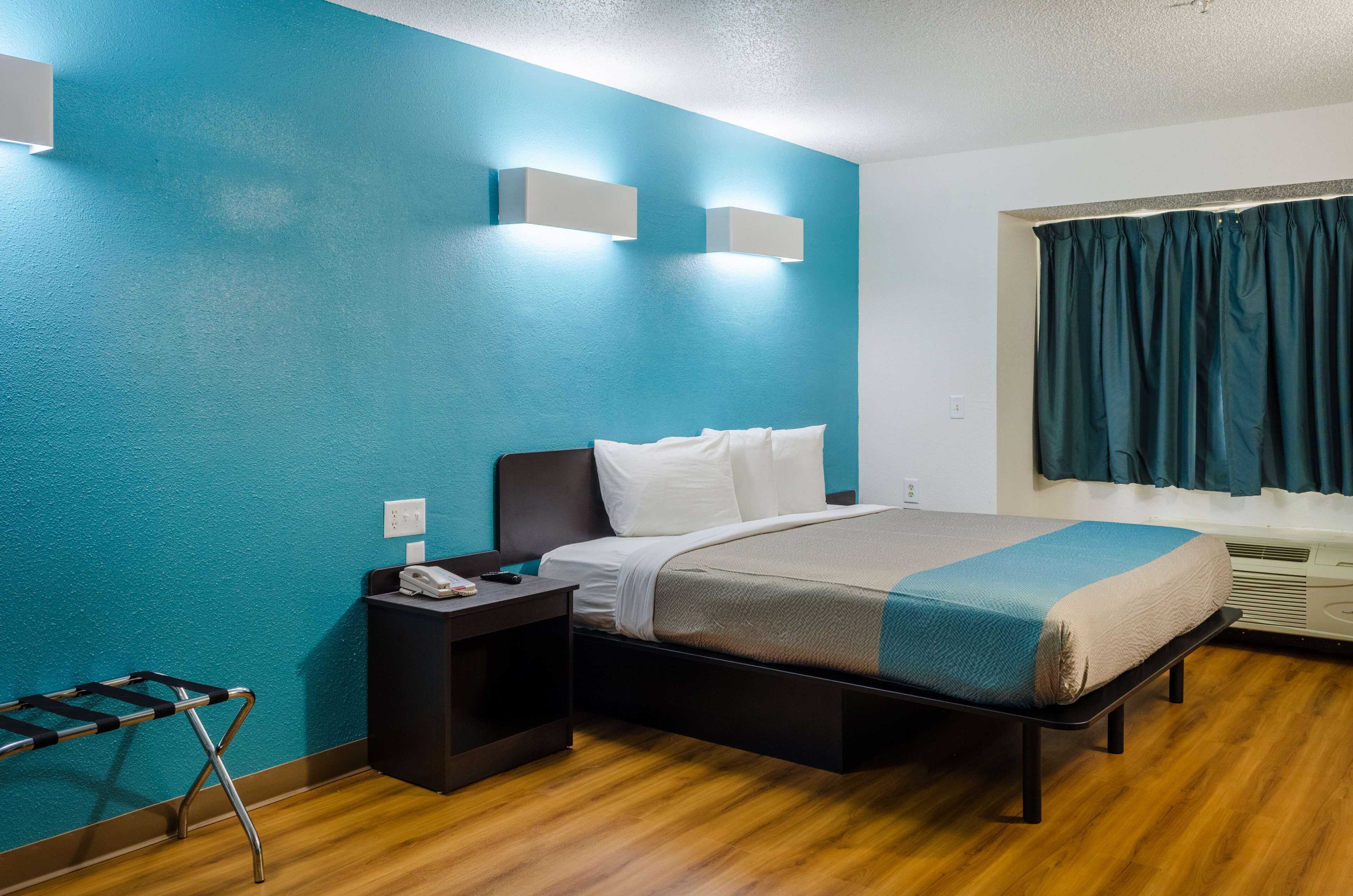A hotel room with a bed, a nightstand, a telephone, and a window with curtains.