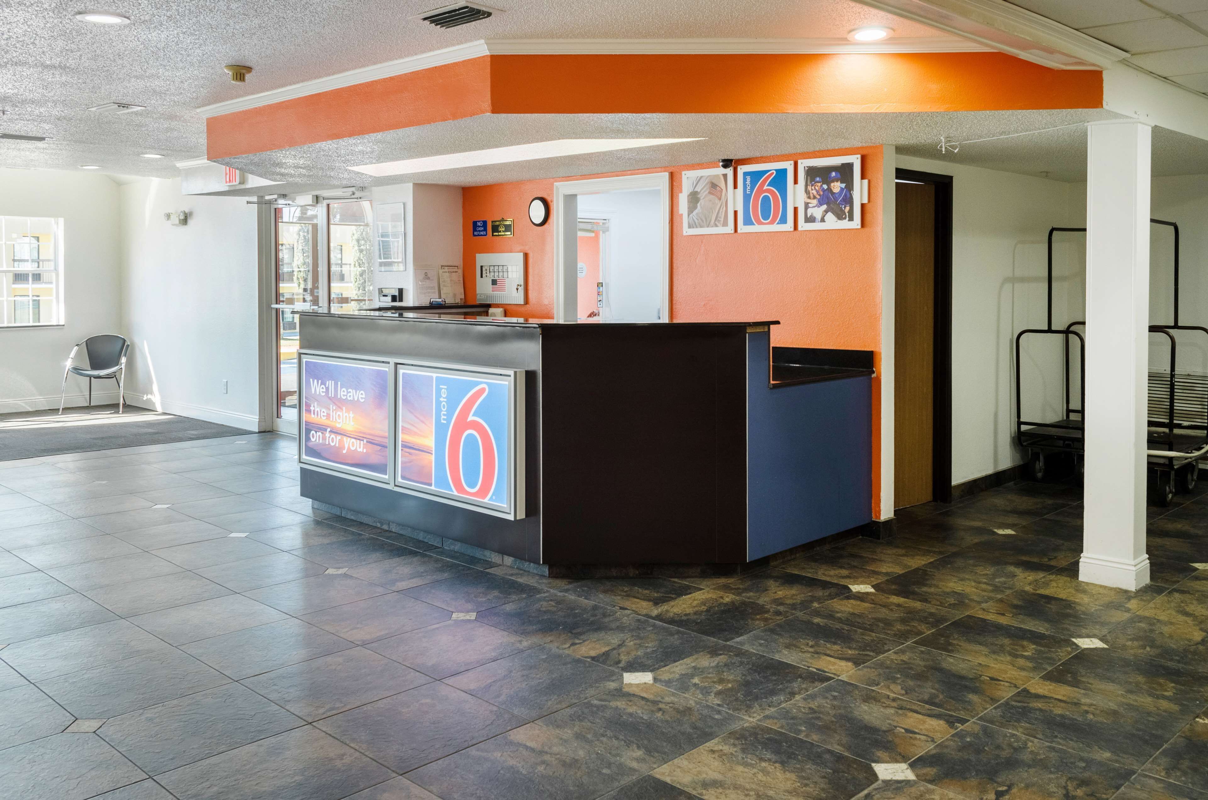 A hotel reception area with a modern design, featuring a reception desk, a digital display, and a view of the outside.