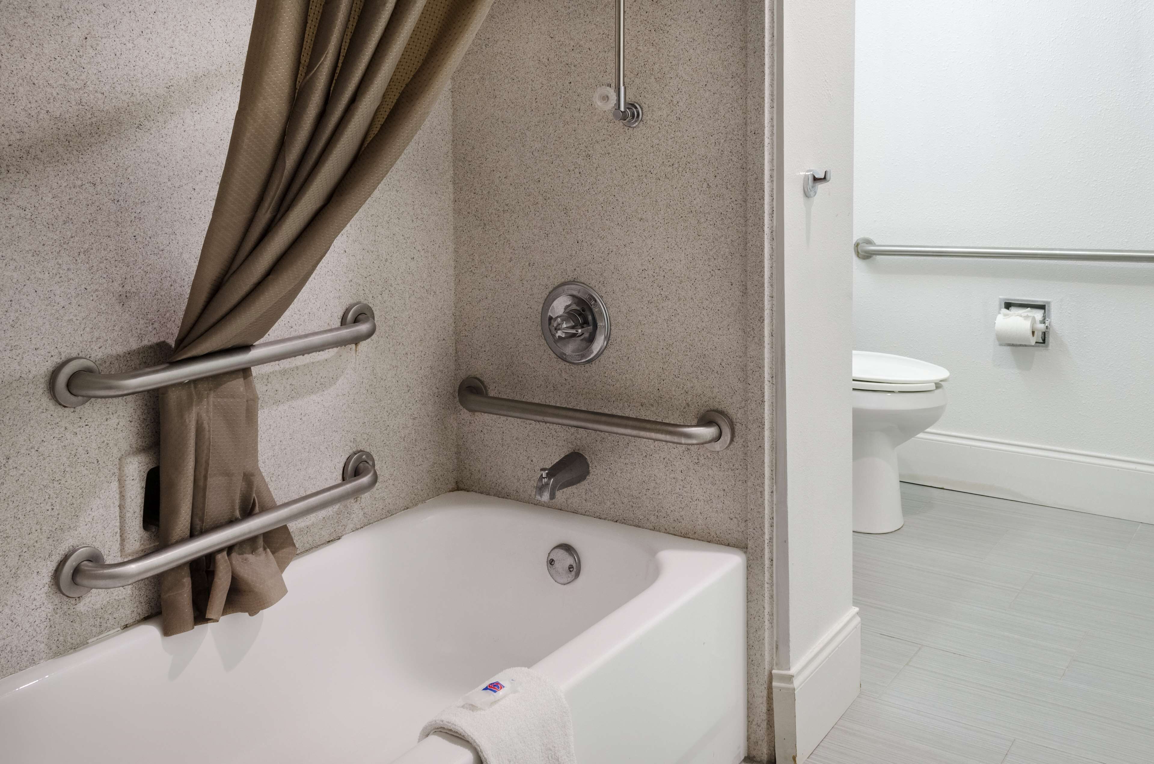 Un baño con bañera, barras de apoyo, inodoro y cortina de ducha.