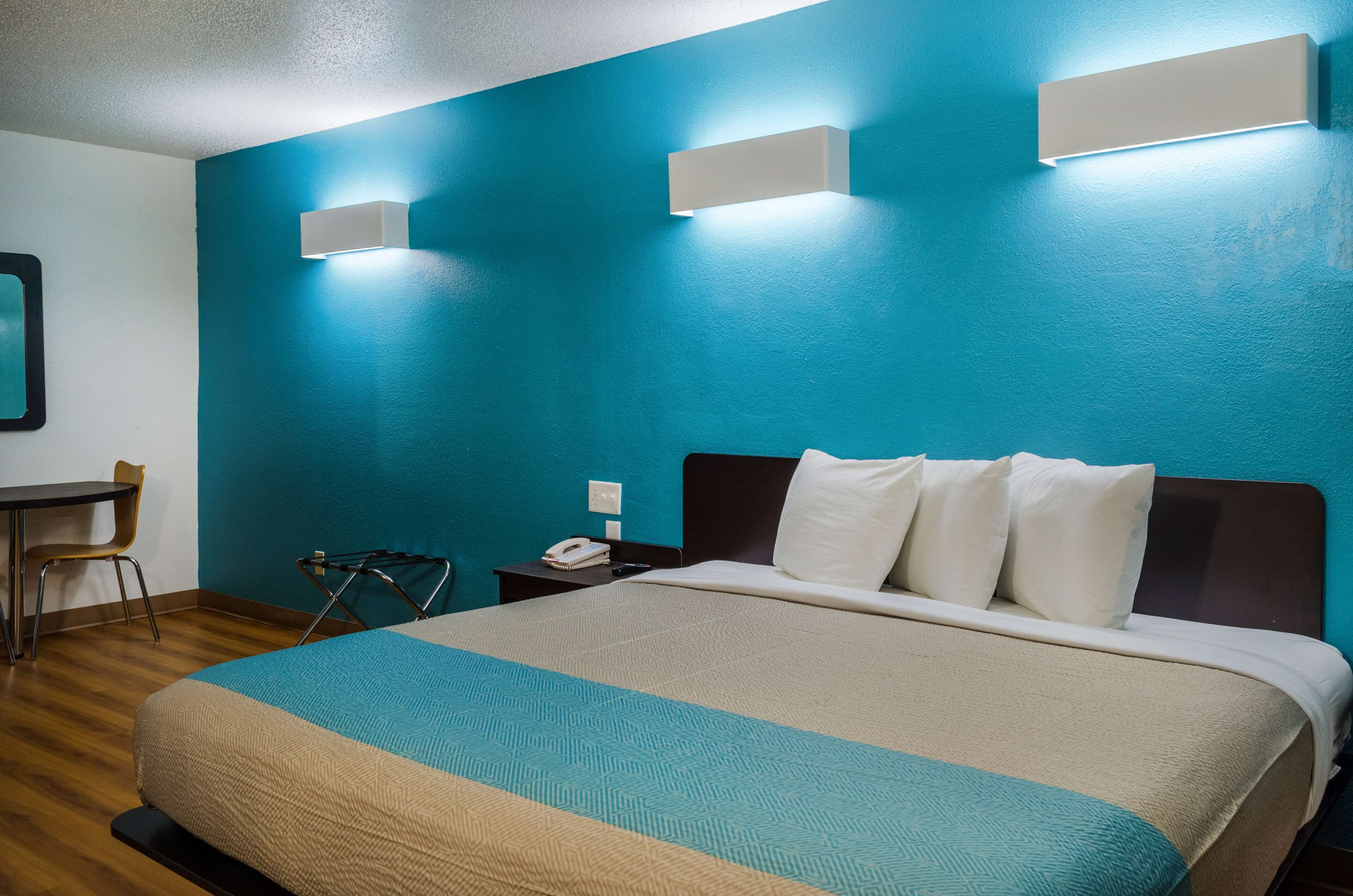 A hotel room with a large bed, a desk, and a chair. There are two wall-mounted lights and a phone on the nightstand.