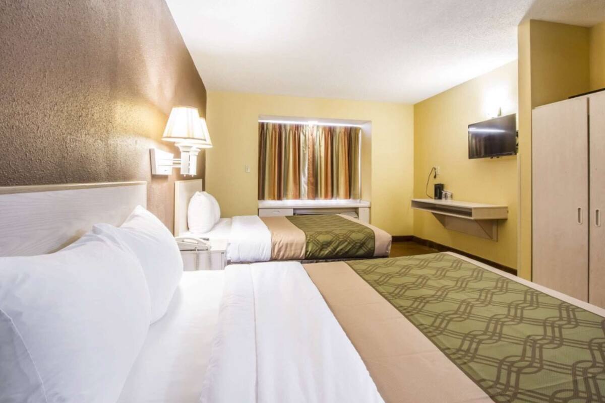 Habitación de hotel con cama, mesita de noche con lámpara, televisor en la pared y armario.
