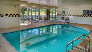A swimming pool with a lifebuoy on the wall, poolside chairs, and a sign with pool rules.