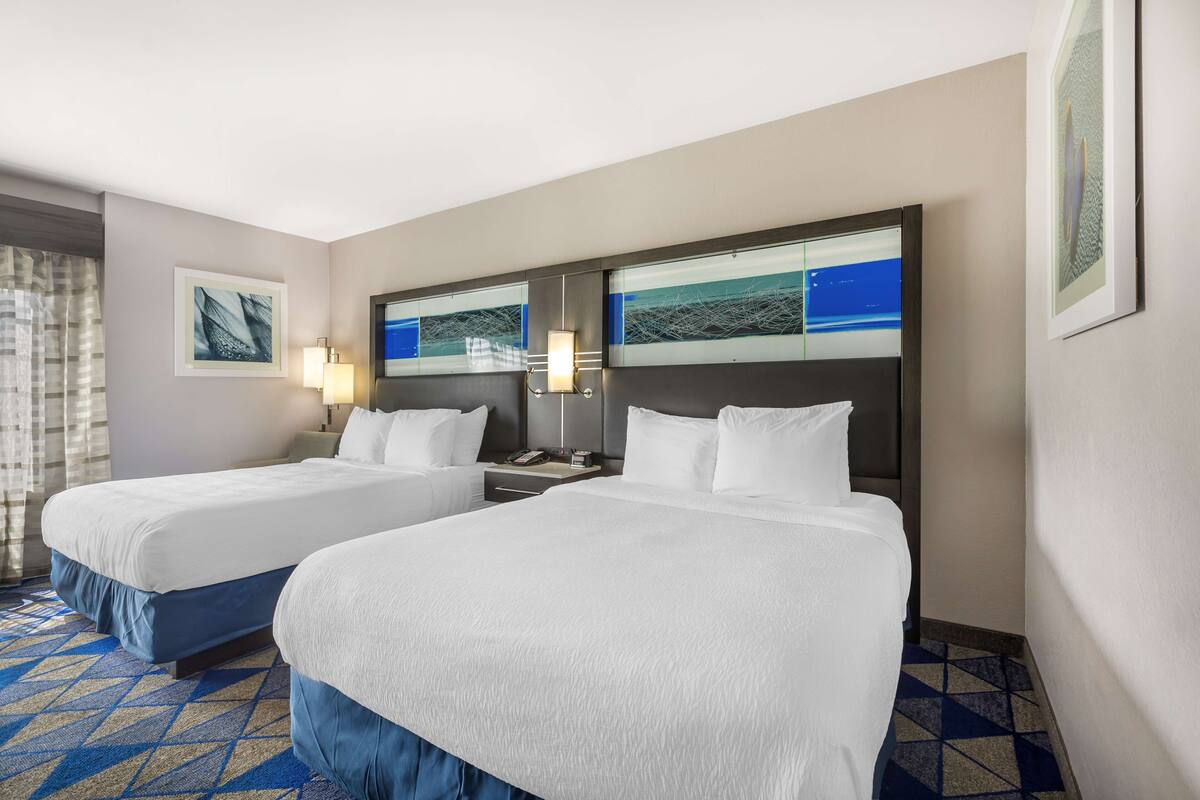 A hotel room with two beds, a nightstand, and a wall-mounted TV.