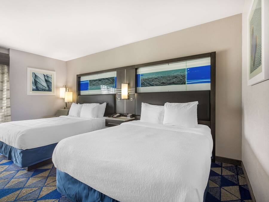 A hotel room with two beds, a nightstand, and a wall-mounted TV.