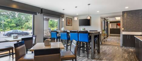 Un restaurante moderno con zona de bar, amplios ventanales y cocina visible al fondo.