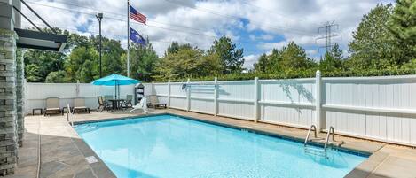 Una piscina rectangular con solárium de piedra, valla blanca y asta con la bandera estadounidense.