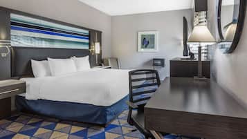 A hotel room with a bed, desk, chair, and a large mirror.