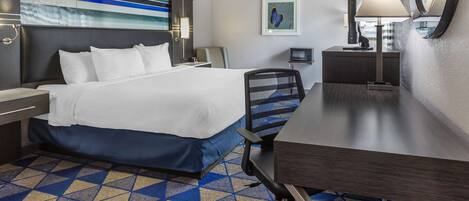 Une chambre d’hôtel avec un lit, un bureau, une chaise et un grand miroir.