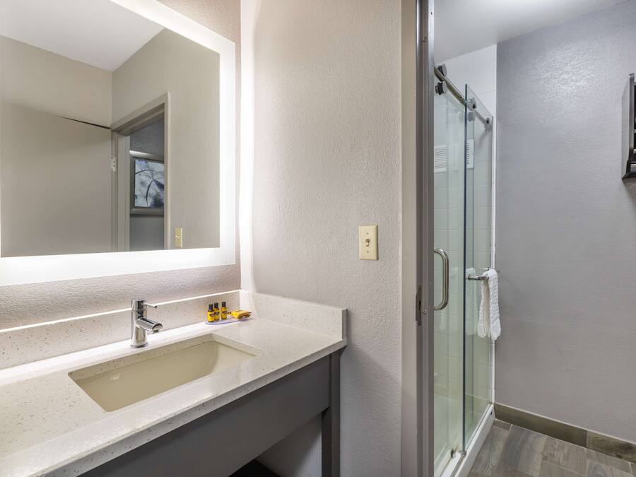 Un bany amb un mirall gran, un lavabo i una cabina de dutxa de vidre.