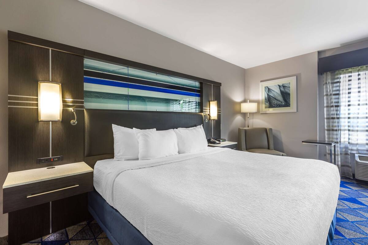 A hotel room with a large bed, a desk, a chair, and a window with curtains.