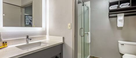 Un baño con un espejo grande, un lavabo, cabina de ducha de vidrio y un inodoro.