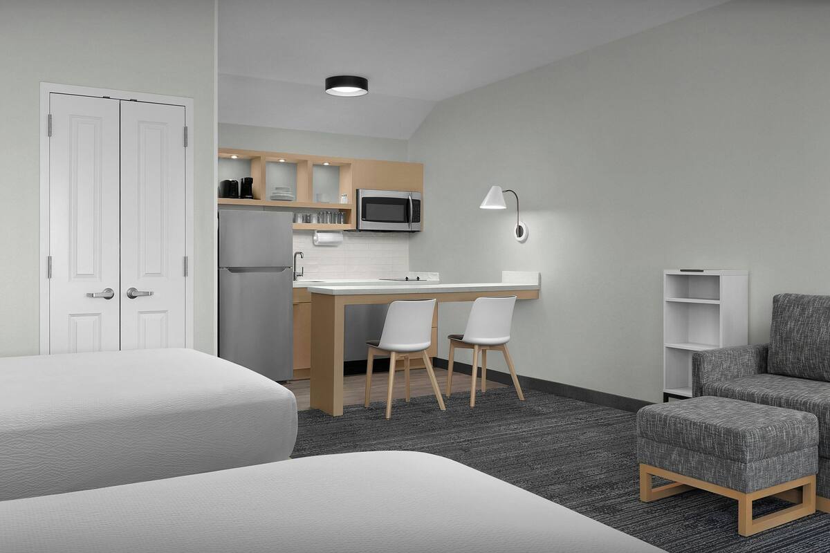 Una habitación de hotel compacta con kitchenette, un escritorio con dos sillas, un sofá y una cama.