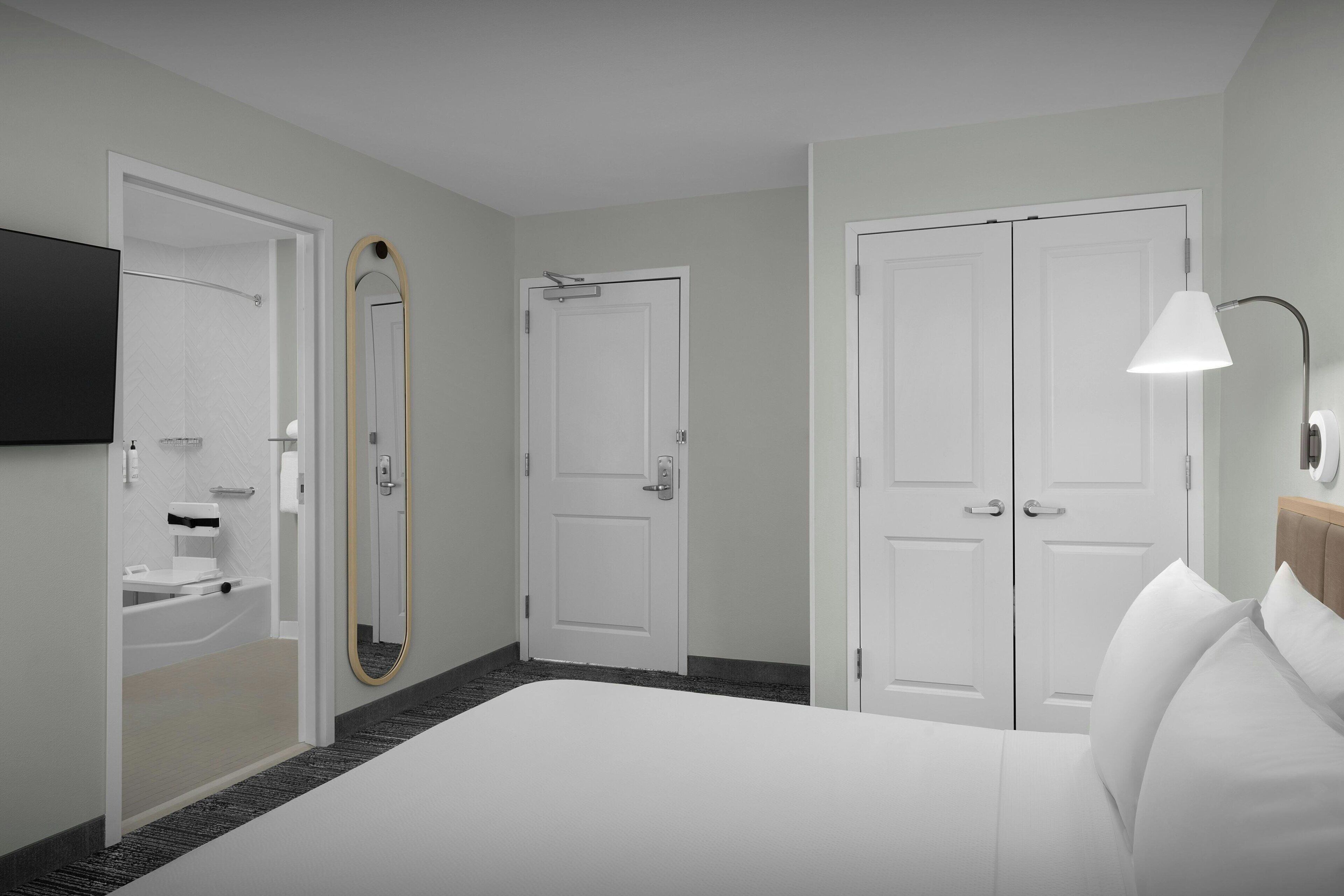 A hotel room with a bed, a bathroom with a sink and mirror, and two doors.