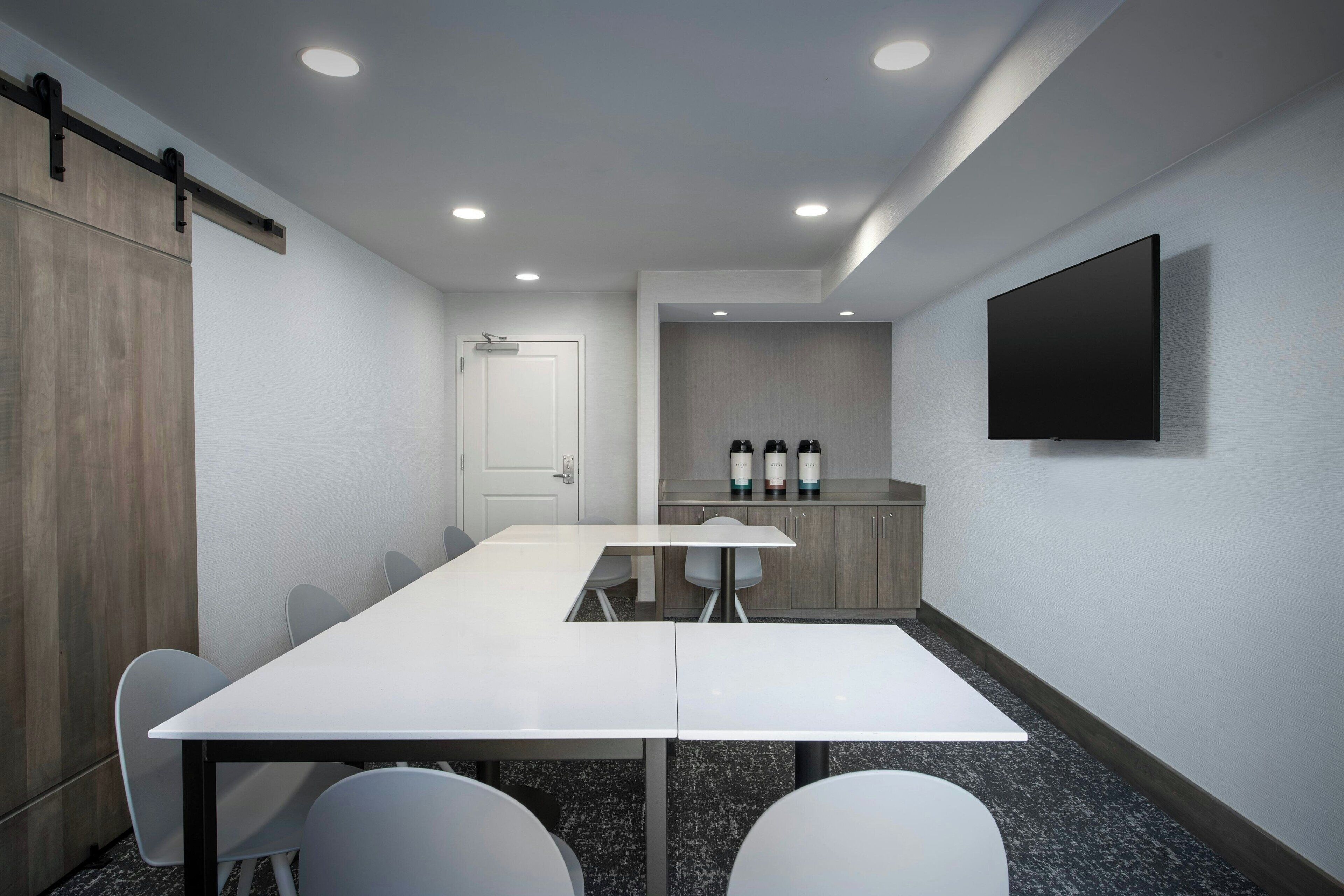 A conference room with a long table, chairs, a whiteboard, and a flat-screen TV mounted on the wall.