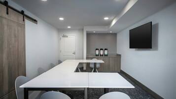 A conference room with a long table, chairs, a whiteboard, and a flat-screen TV mounted on the wall.