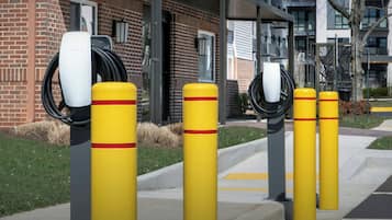 A row of yellow bollards with red stripes, a Tesla charging station, and a brick building with windows and balconies.
