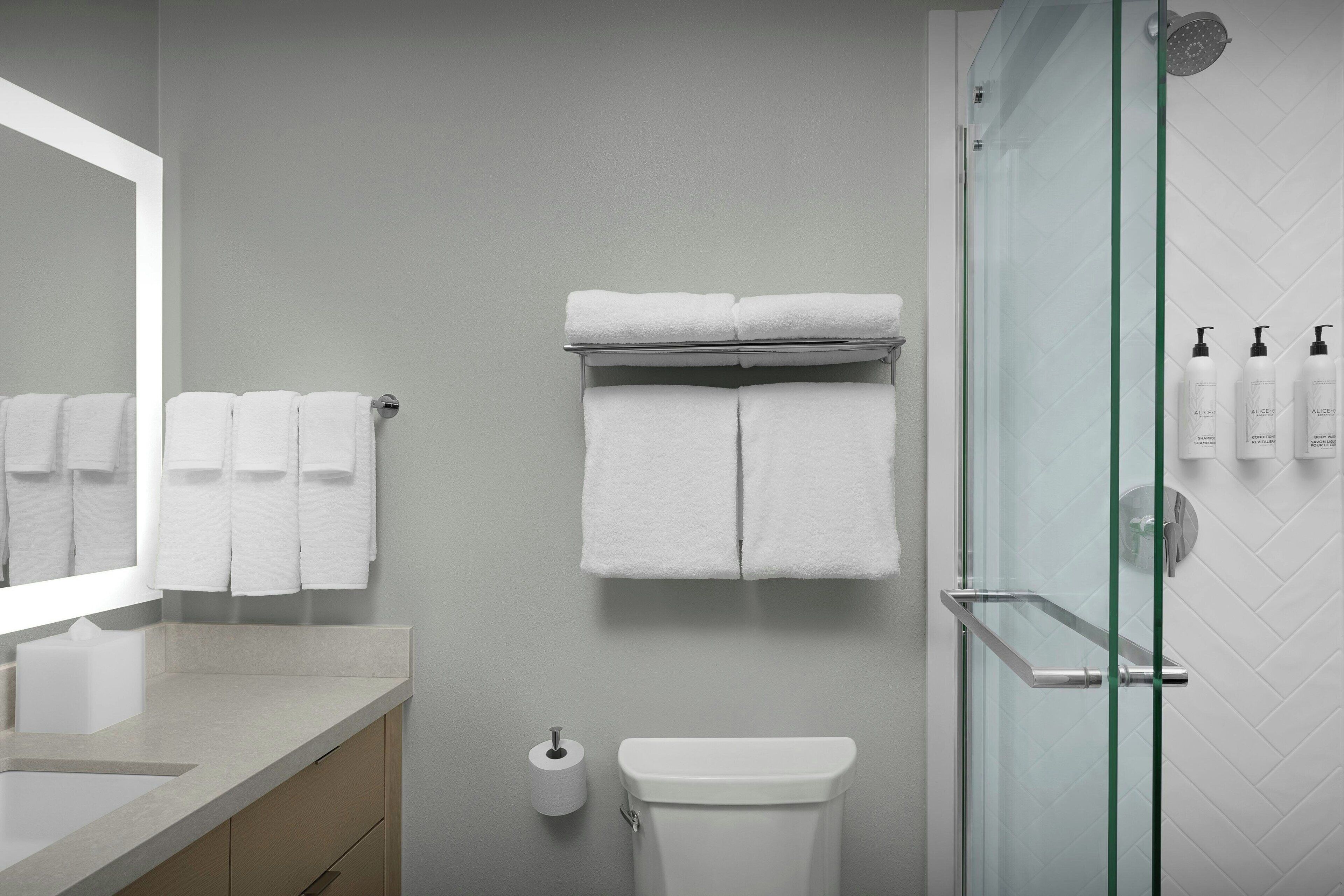 A bathroom with a glass shower enclosure, a toilet, a sink with a mirror, and a towel rack with multiple towels.