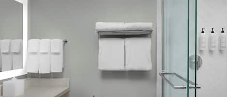 A bathroom with a glass shower enclosure, a toilet, a sink with a mirror, and a towel rack with multiple towels.