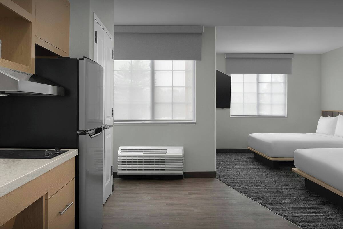 Habitación de hotel moderna con kitchenette, dos camas, un ventanal grande y aire acondicionado instalado.