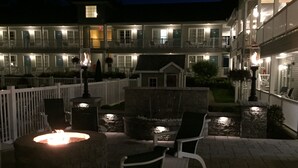 A patio area with a stone fire pit, white outdoor furniture, and a white picket fence. - Quality Inn Lake George (Lake George)